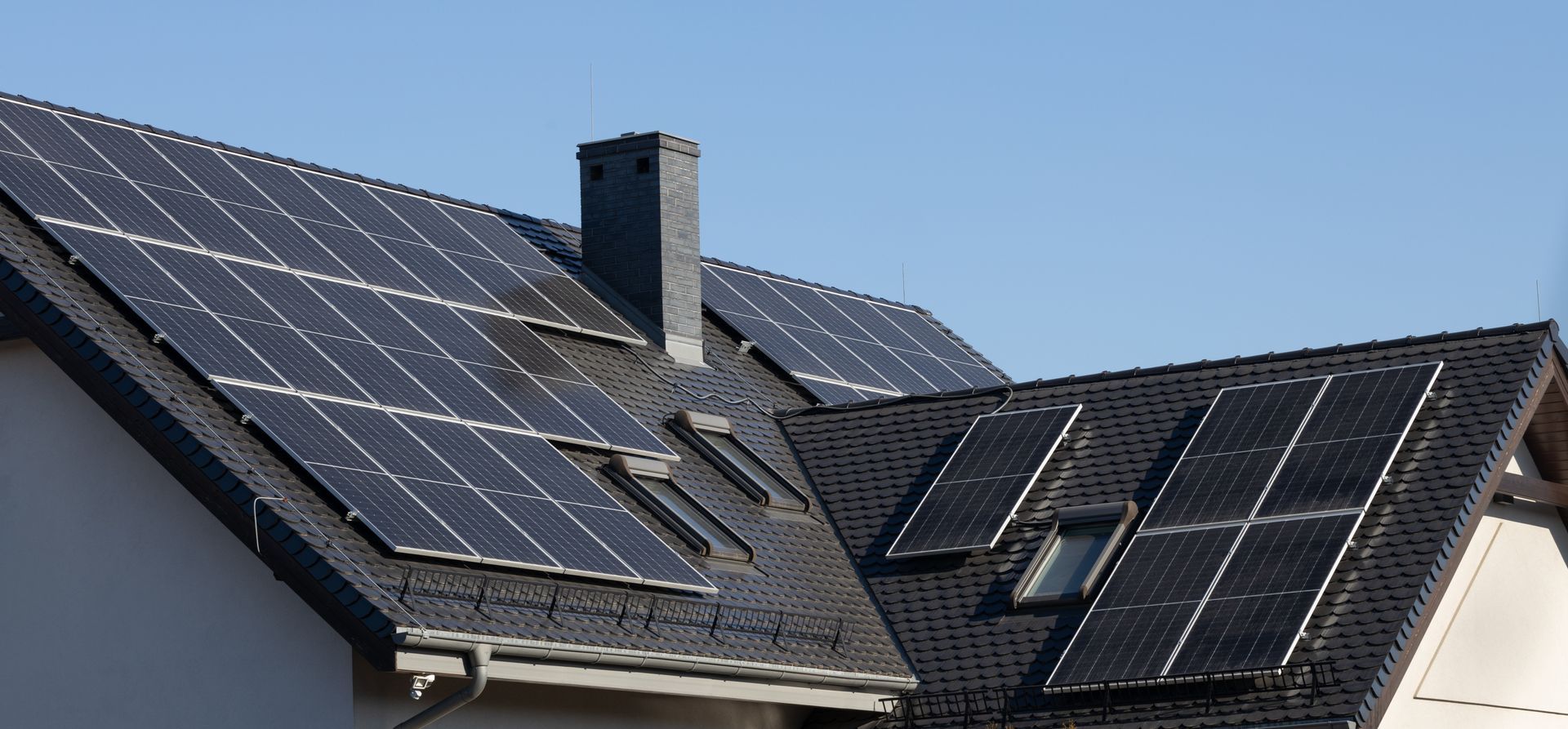 Solar panels on a house roof with a chimney, under a blue sky.