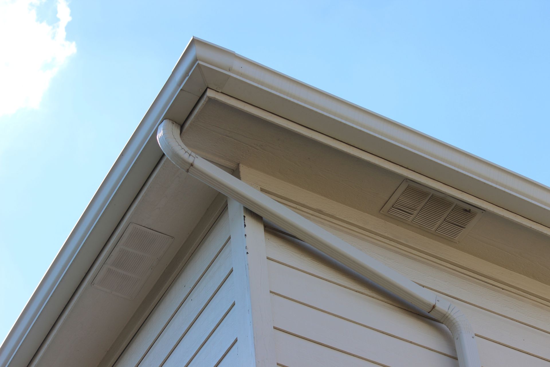 Corner of a house with white siding and gutters against a blue sky.
