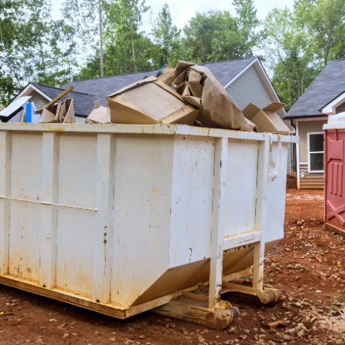 A white dumpster filled with cardboard boxes in front of a house