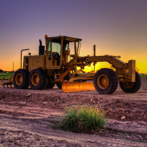 A bulldozer is parked in a dirt field at sunset