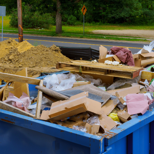 A blue dumpster filled with lots of cardboard and wood.