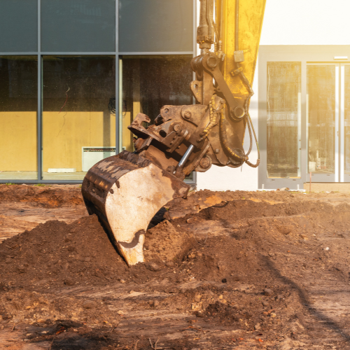 An excavator is digging a hole in the ground in front of a building.