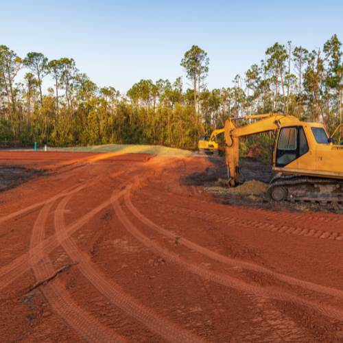 A yellow excavator is digging a hole in a dirt field.