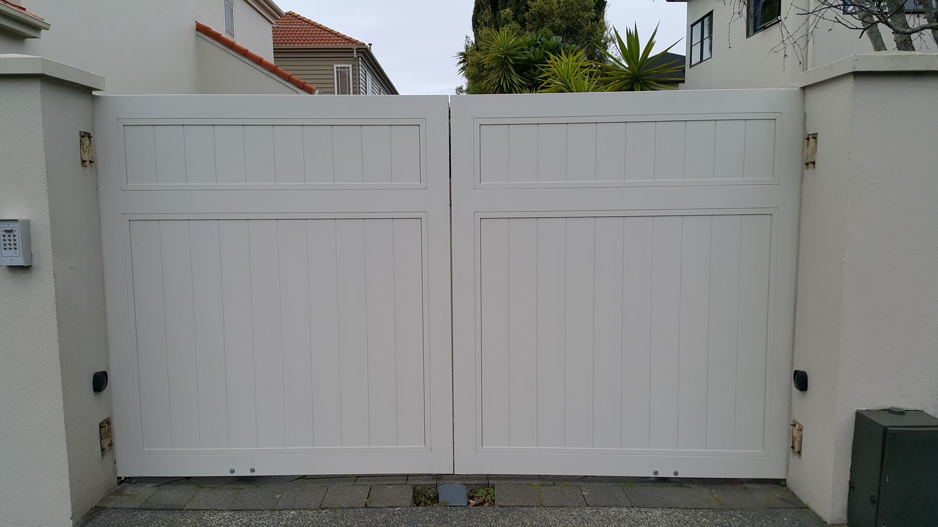 A white gate is open to a driveway in front of a house.