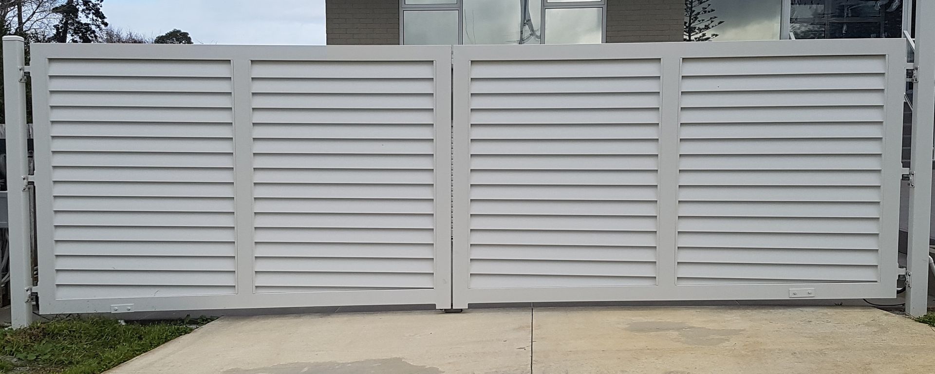A white gate is sitting on top of a concrete driveway in front of a house.