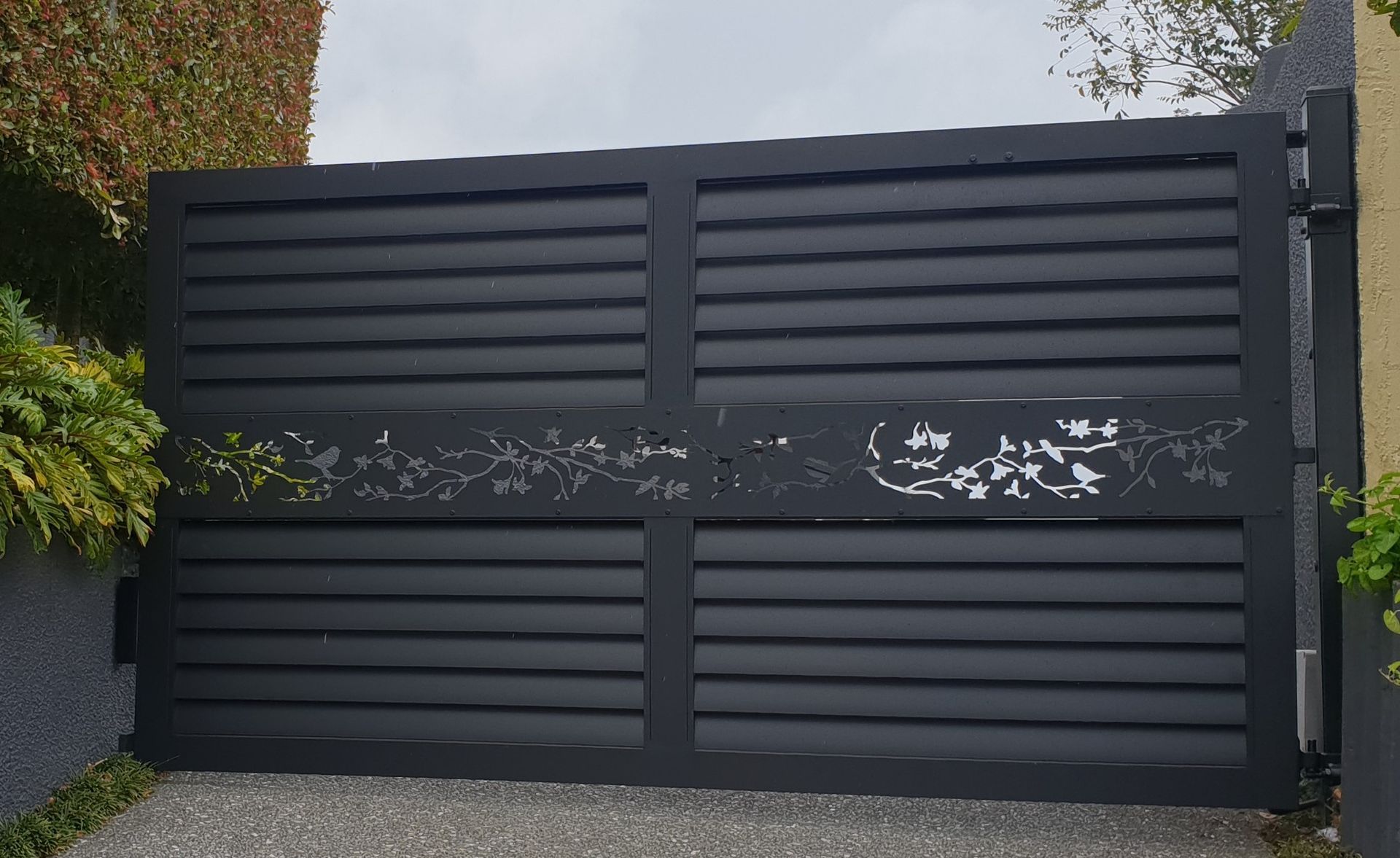 A black gate is open to a gravel driveway.