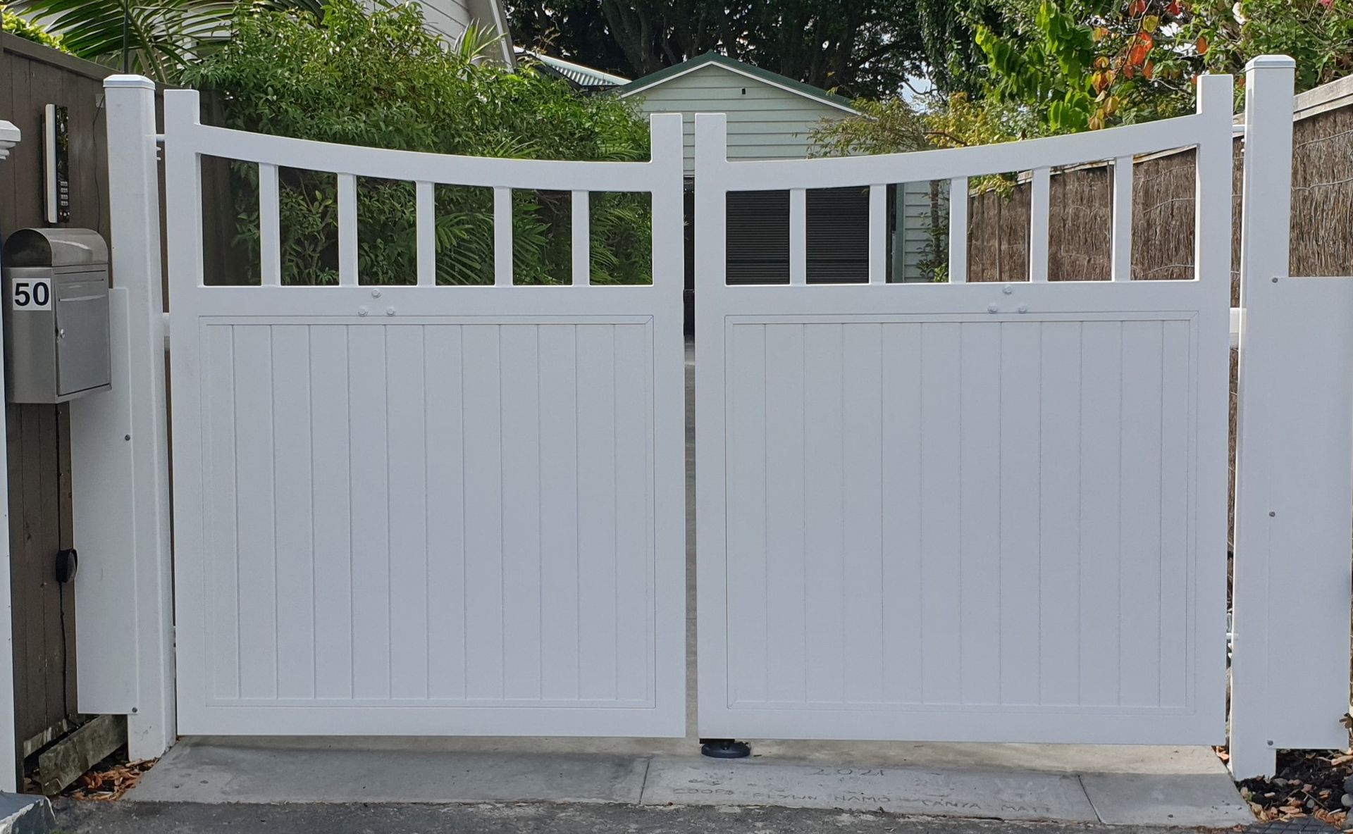 A white gate is open to a driveway in front of a house.