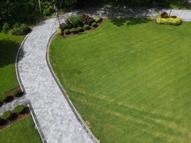 Curved stone garden path beside a green lawn and landscaped shrubs