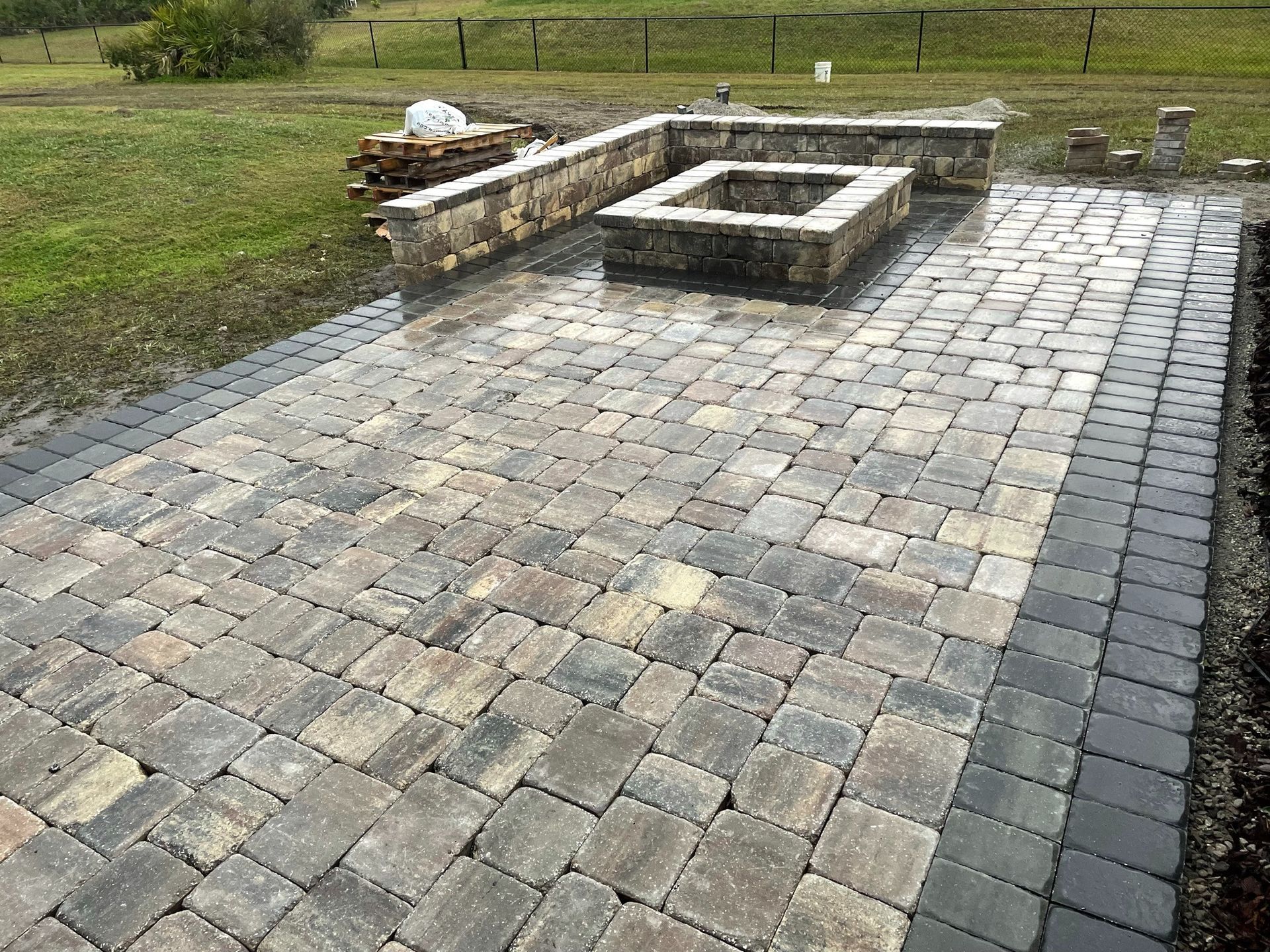 Stone-paved patio with a low concrete fire pit and bench in a grassy yard