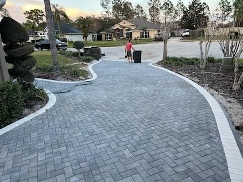 Curved paved walkway in a suburban neighborhood, with a person pushing a trash bin near houses and trees.