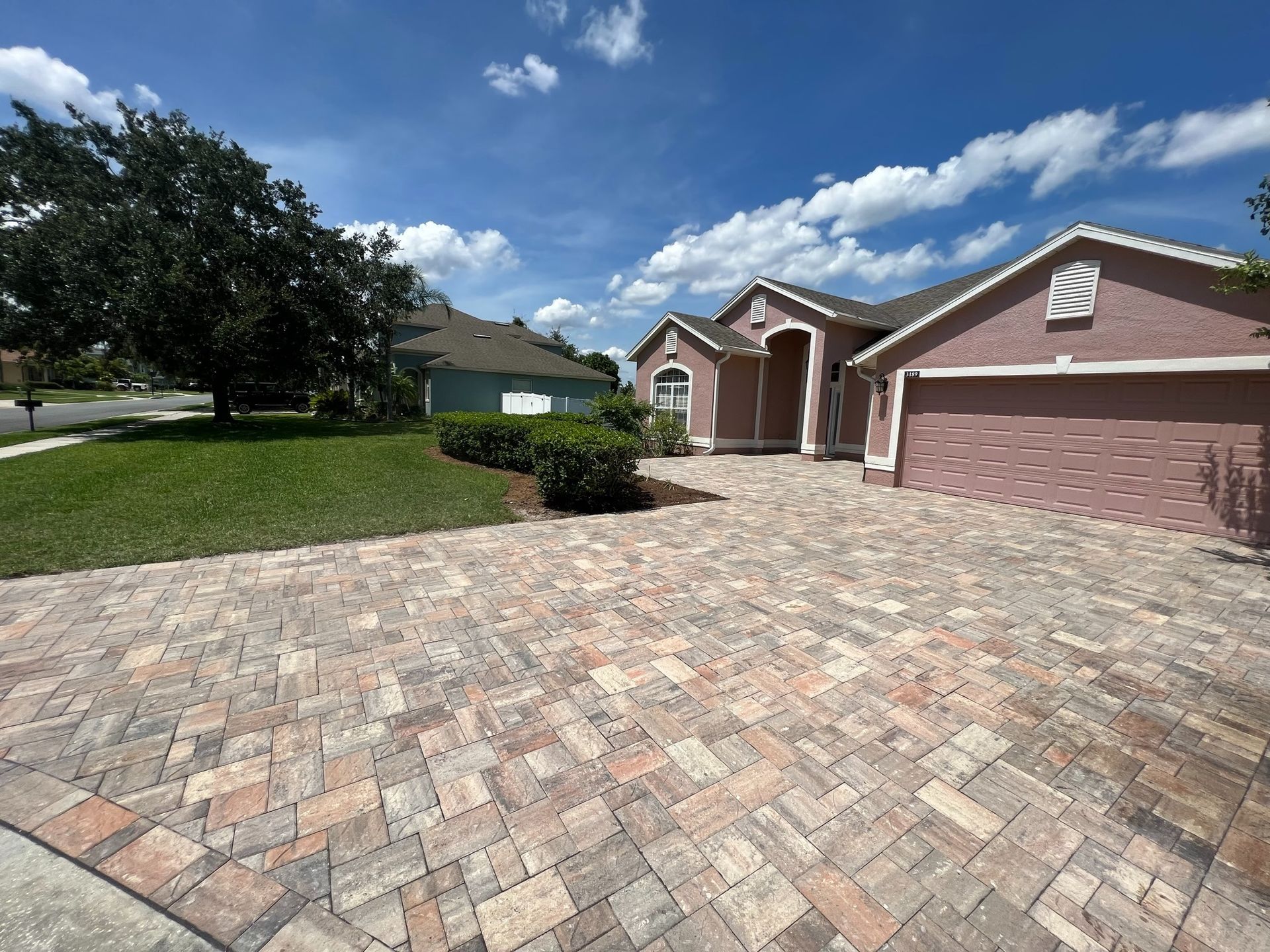 Brick-paver driveway leading to a brick suburban house under a blue sky with clouds