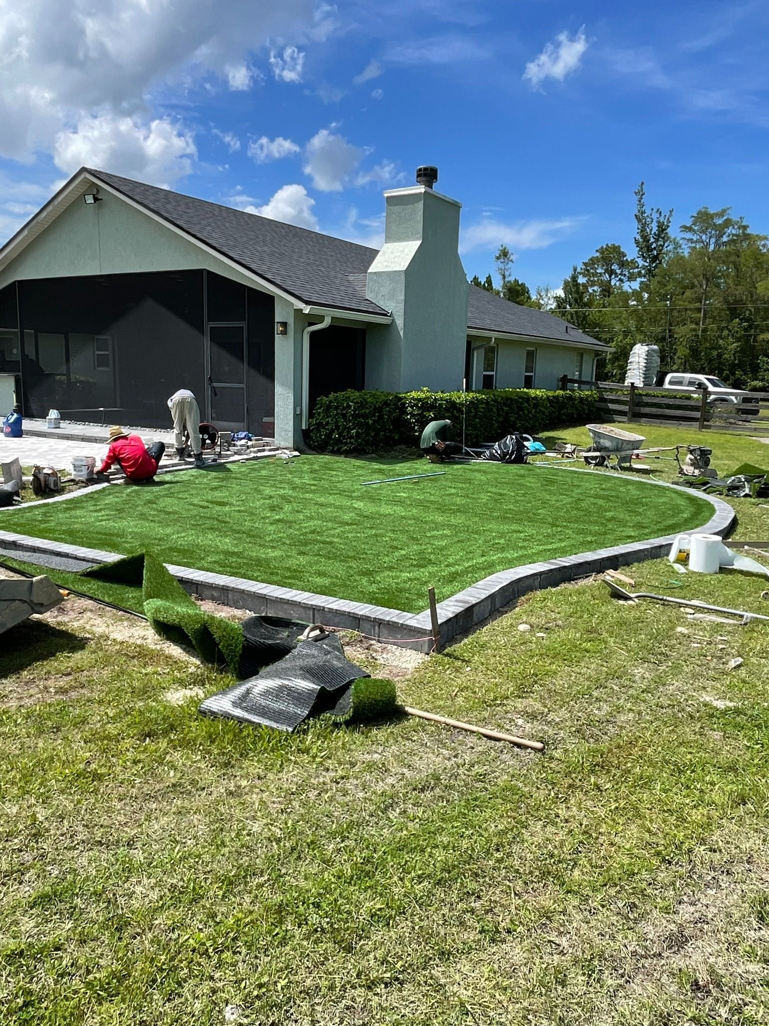 Small house with a white chimney, green lawn, and scattered yard items under a blue sky.