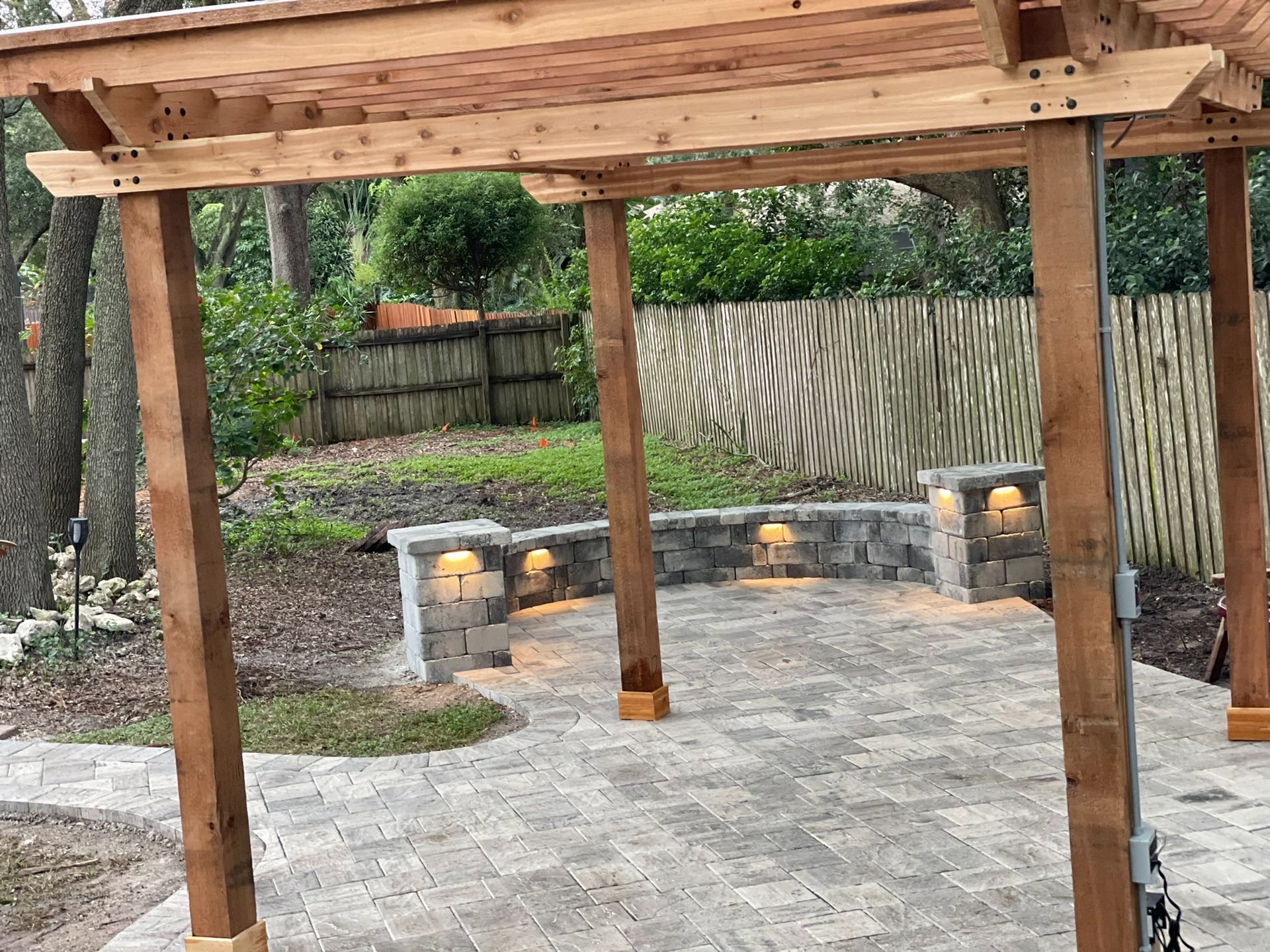 Wooden pergola over a gravel patio with stone benches and a fenced backyard garden
