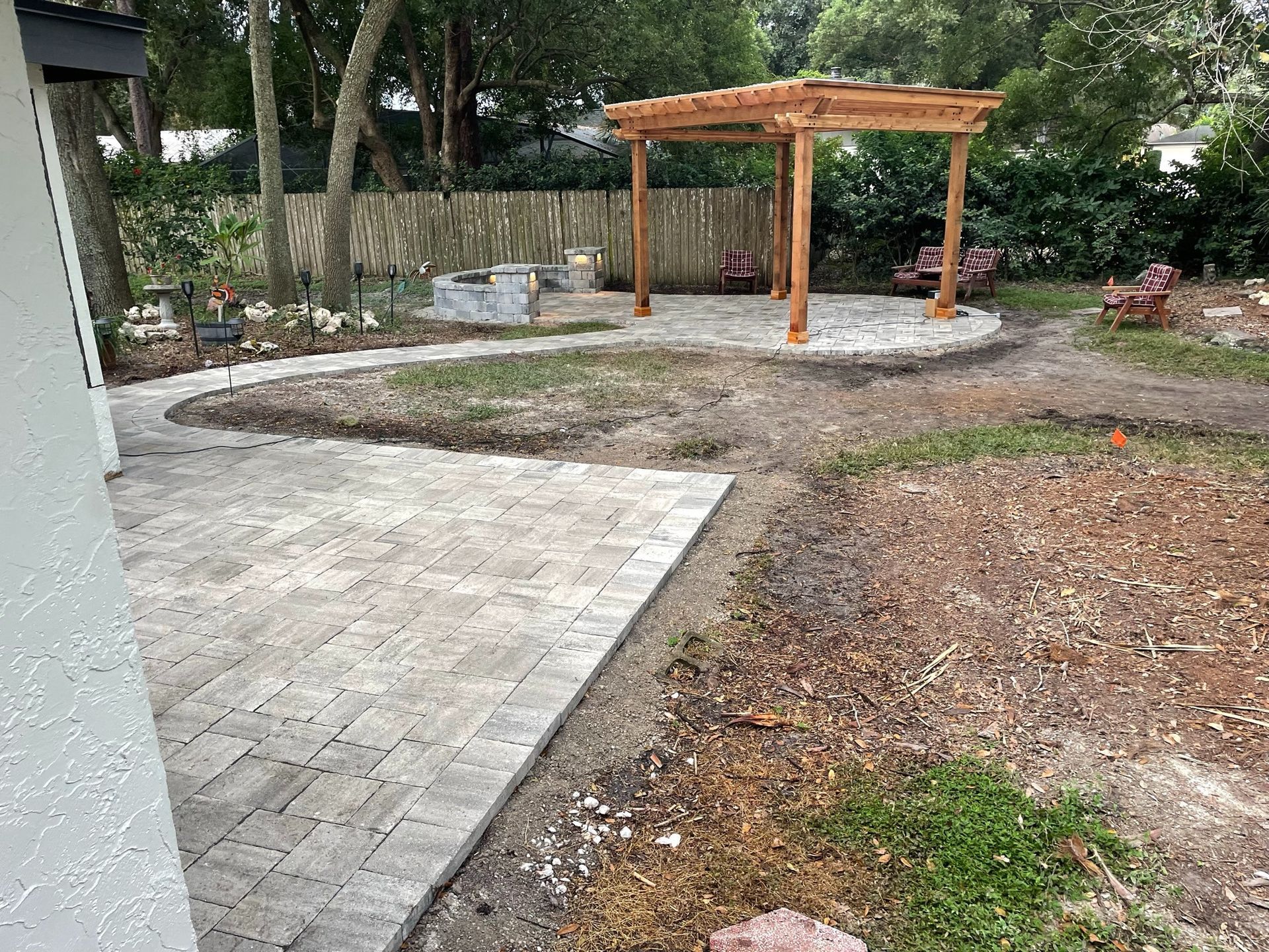 Backyard patio with paved paths, mulch, trees, and a wooden pergola on a circular concrete pad