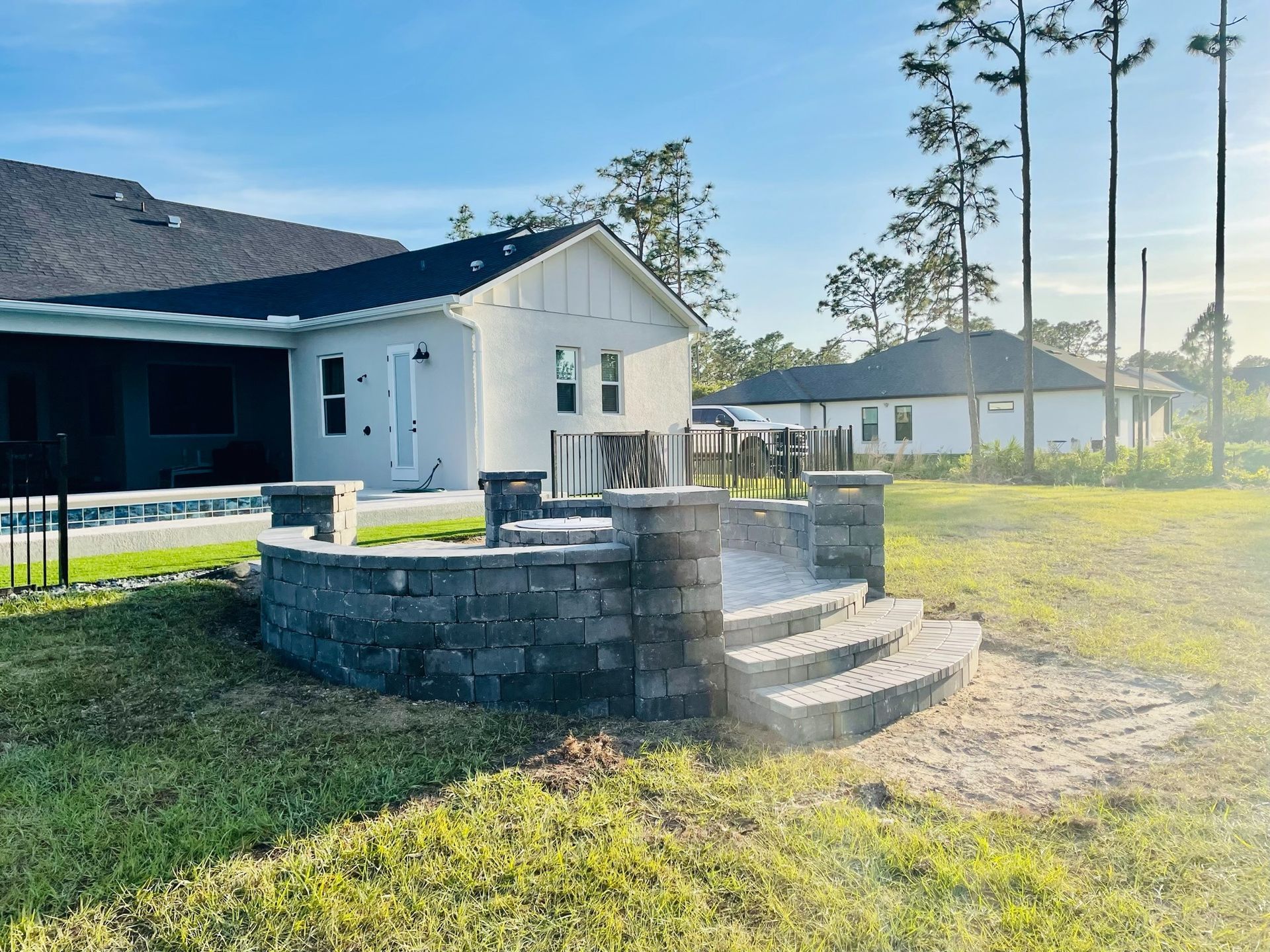 Backyard with stone fire pit, steps, white house, and wooden deck in sunny yard