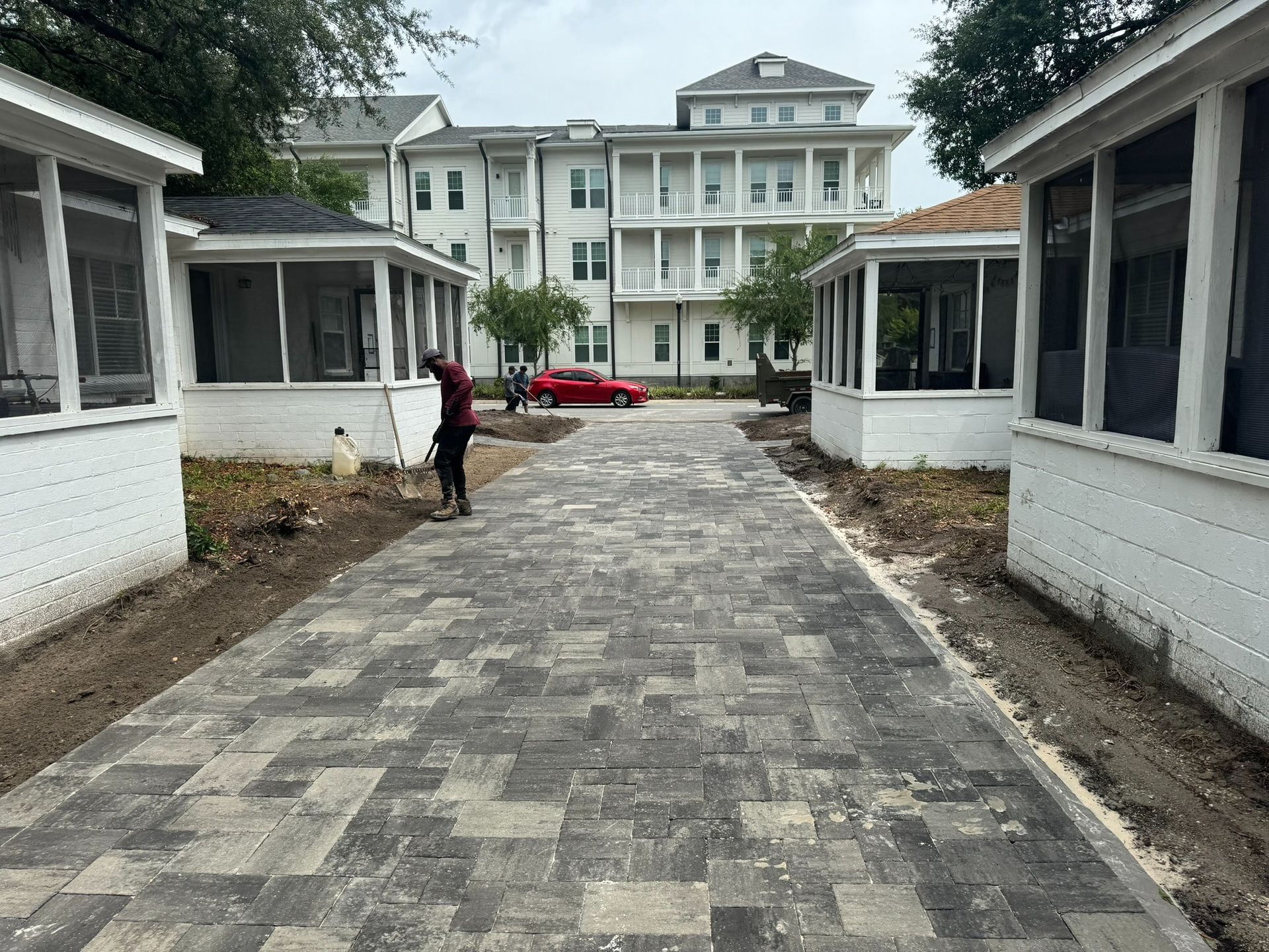 Paved walkway between white buildings leading to a large hotel, with a person and red car ahead