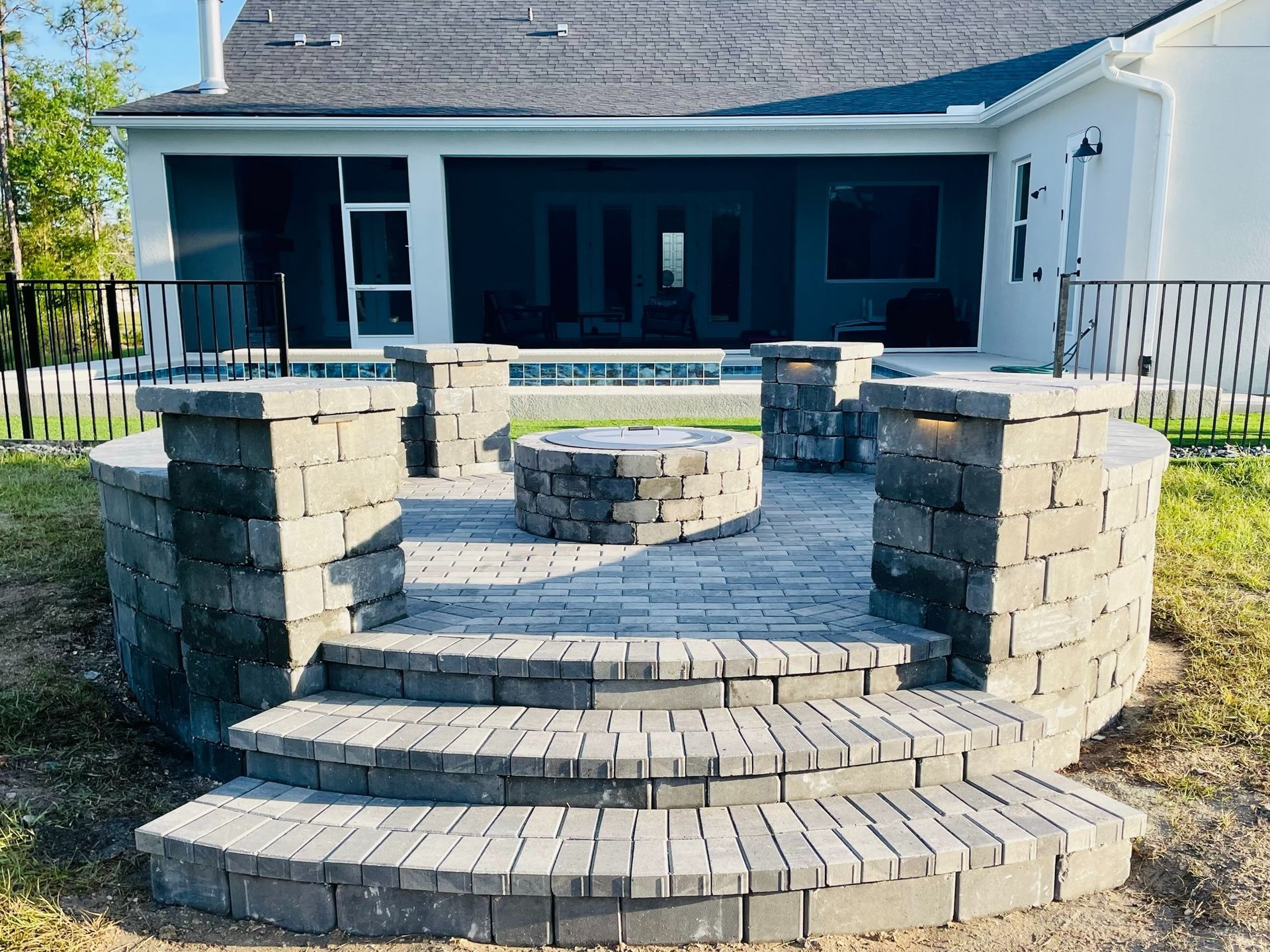 Stone steps and curved brick retaining walls leading to a raised backyard patio with a white house and screened porch.
