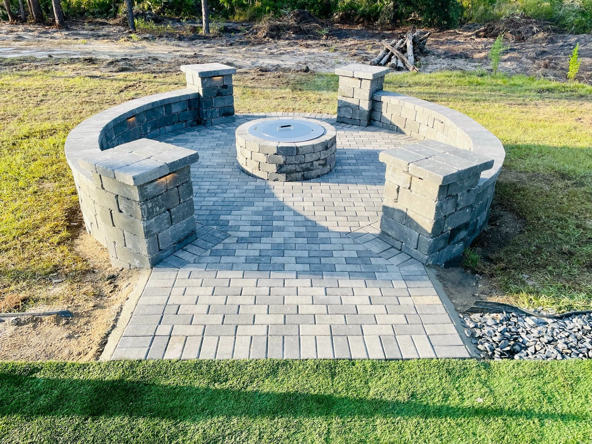 Stone circular seating area with built-in benches and a central fire pit on a paved patio in a grassy yard
