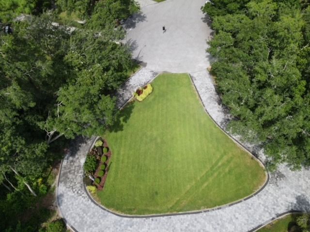 Aerial view of a manicured green lawn surrounded by curved stone paths and dense trees.