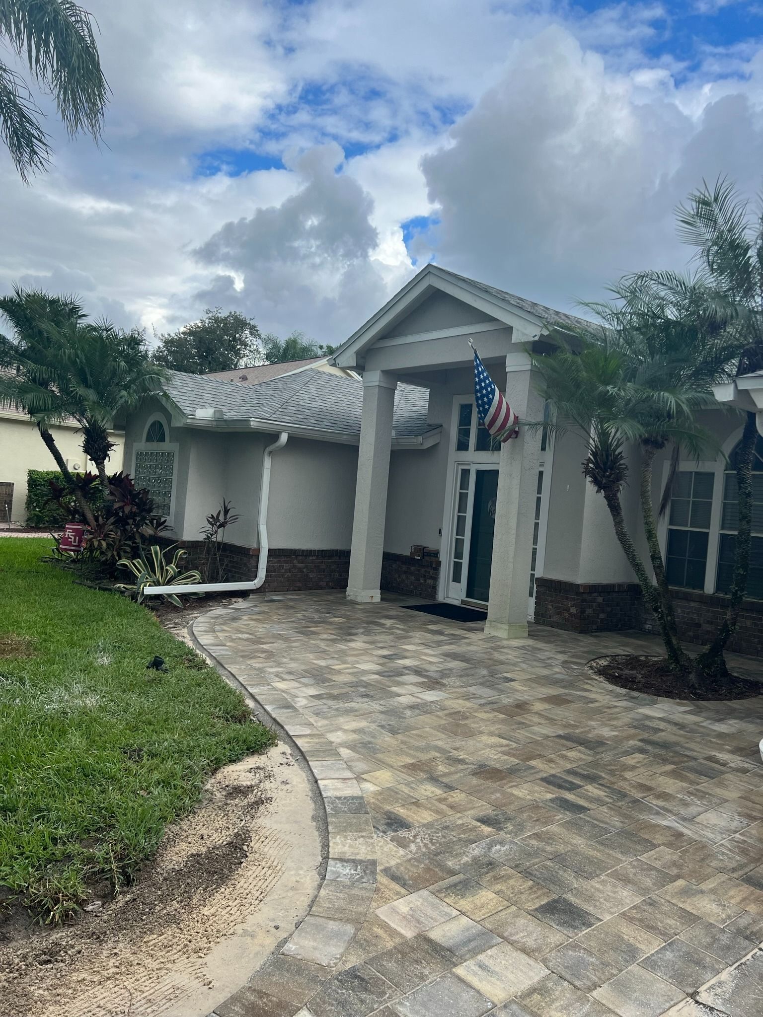 Single-story house with a curved stone driveway, white exterior, and cloudy sky.