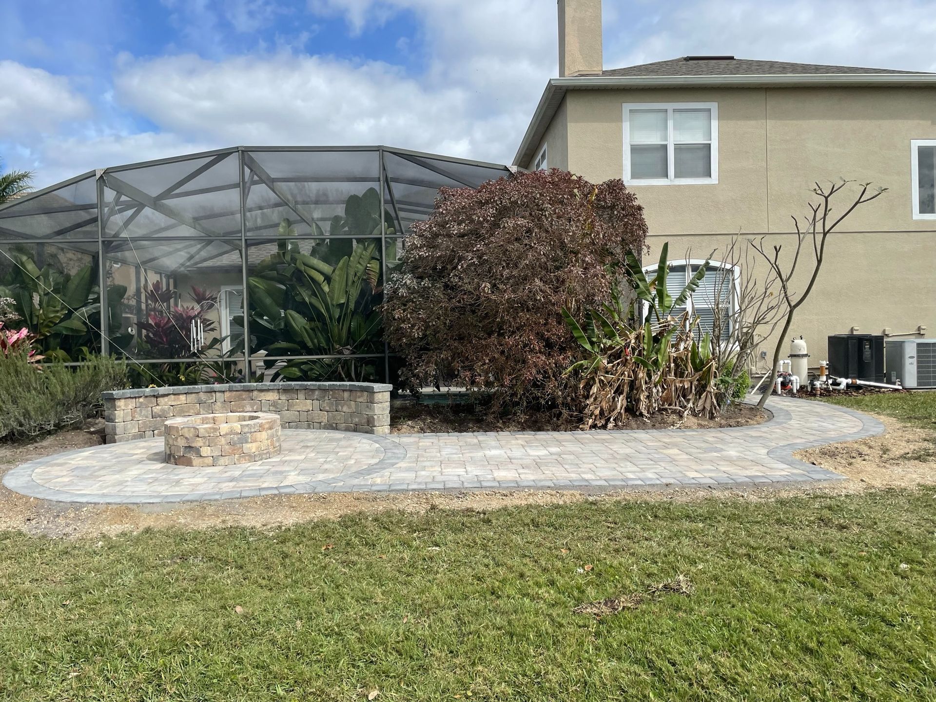 Backyard patio with a screened enclosure, fire pit, shrubs, and a beige house behind it
