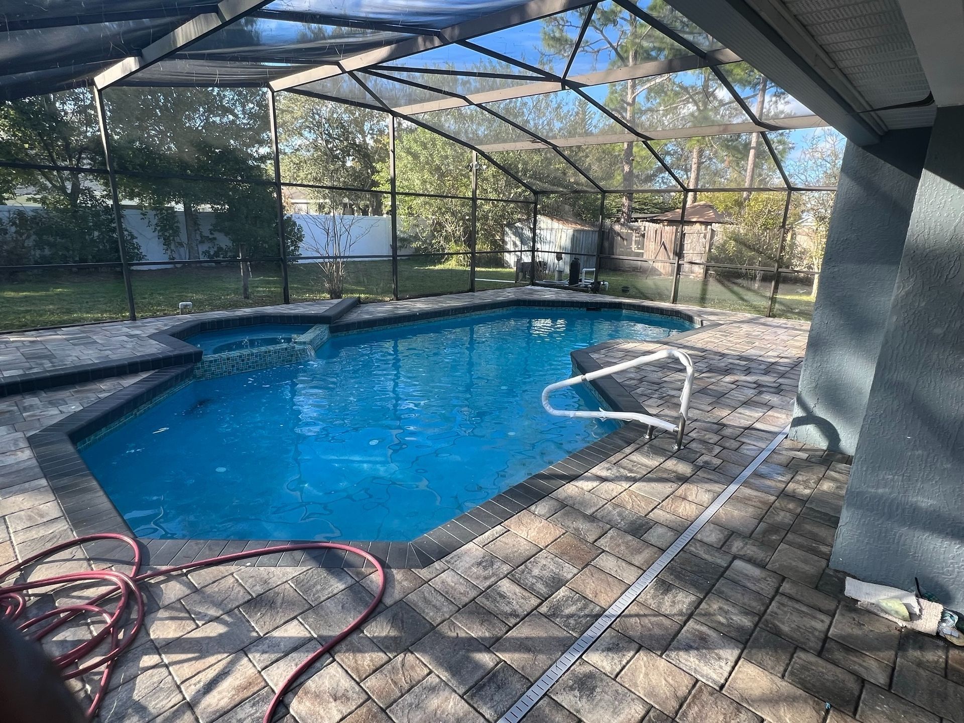 Screened-in backyard pool with blue water, brick pavers, and a garden hose on the patio.