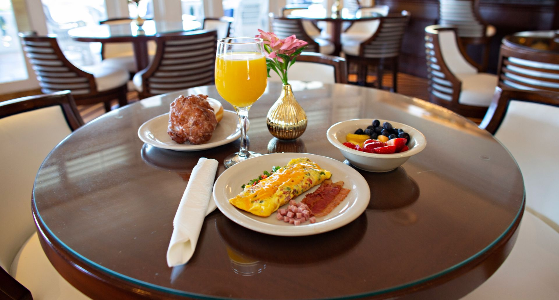 Breakfast plate with eggs, bacon, fruit, pastry, orange juice, and coffee on a restaurant table