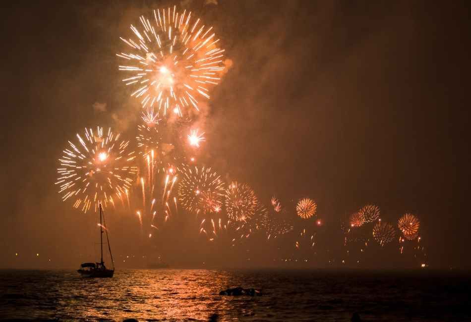 A boat is floating in the water while fireworks are displayed in the sky above it.