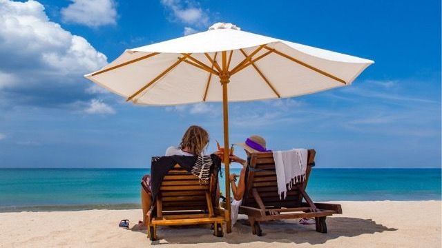 Two people are sitting under an umbrella on the beach.