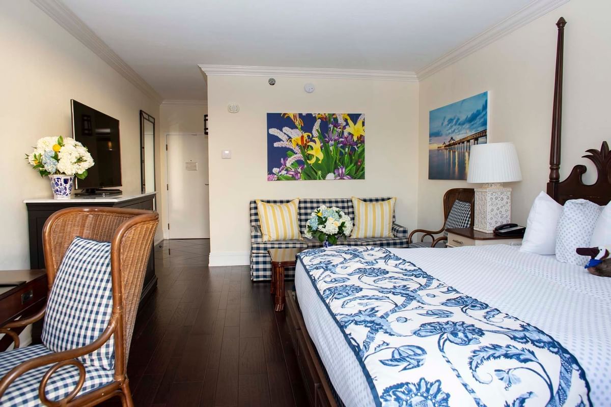 A hotel room with a king size bed , chairs , and a painting on the wall.