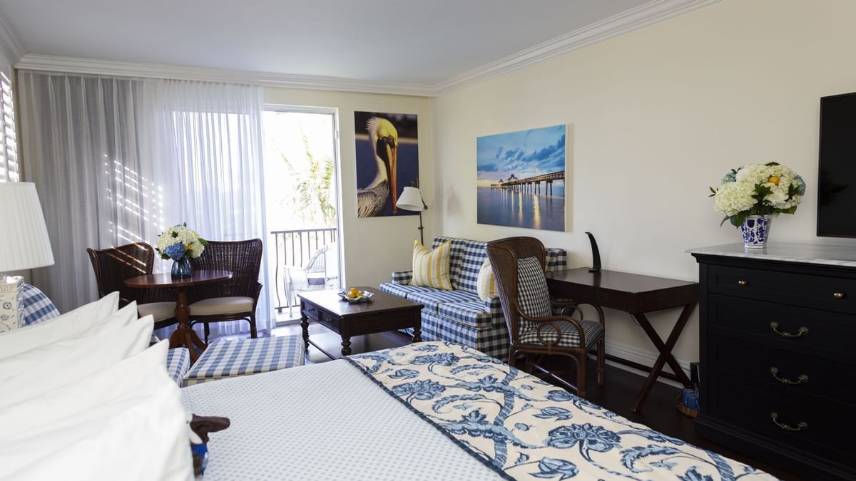 A hotel room with a king size bed , dresser , chairs , table and television.