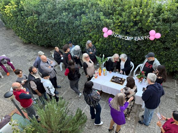 In un giardino, le persone si sono riunite attorno a un tavolo all'aperto con torta e palloncini rosa.