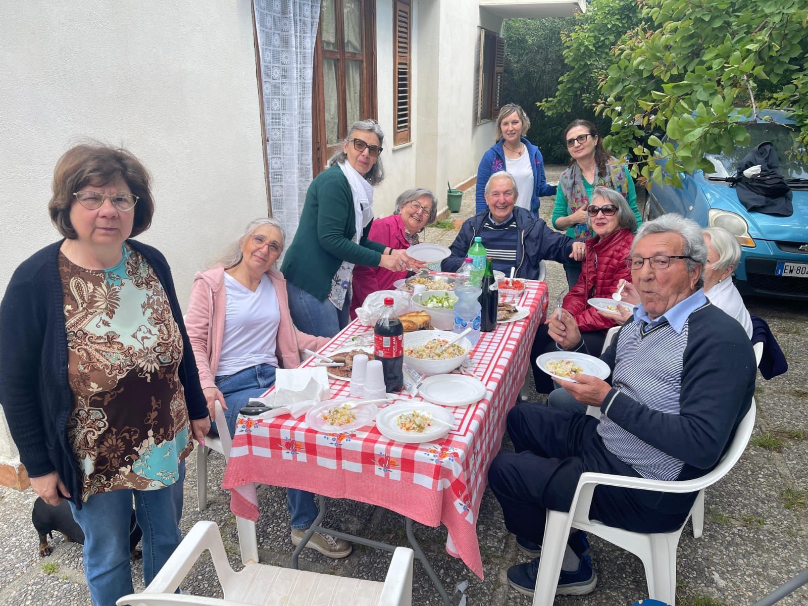 In un cortile, le persone si sono riunite attorno a un tavolo a scacchi rossi all'aperto, condividendo cibo e bevande.