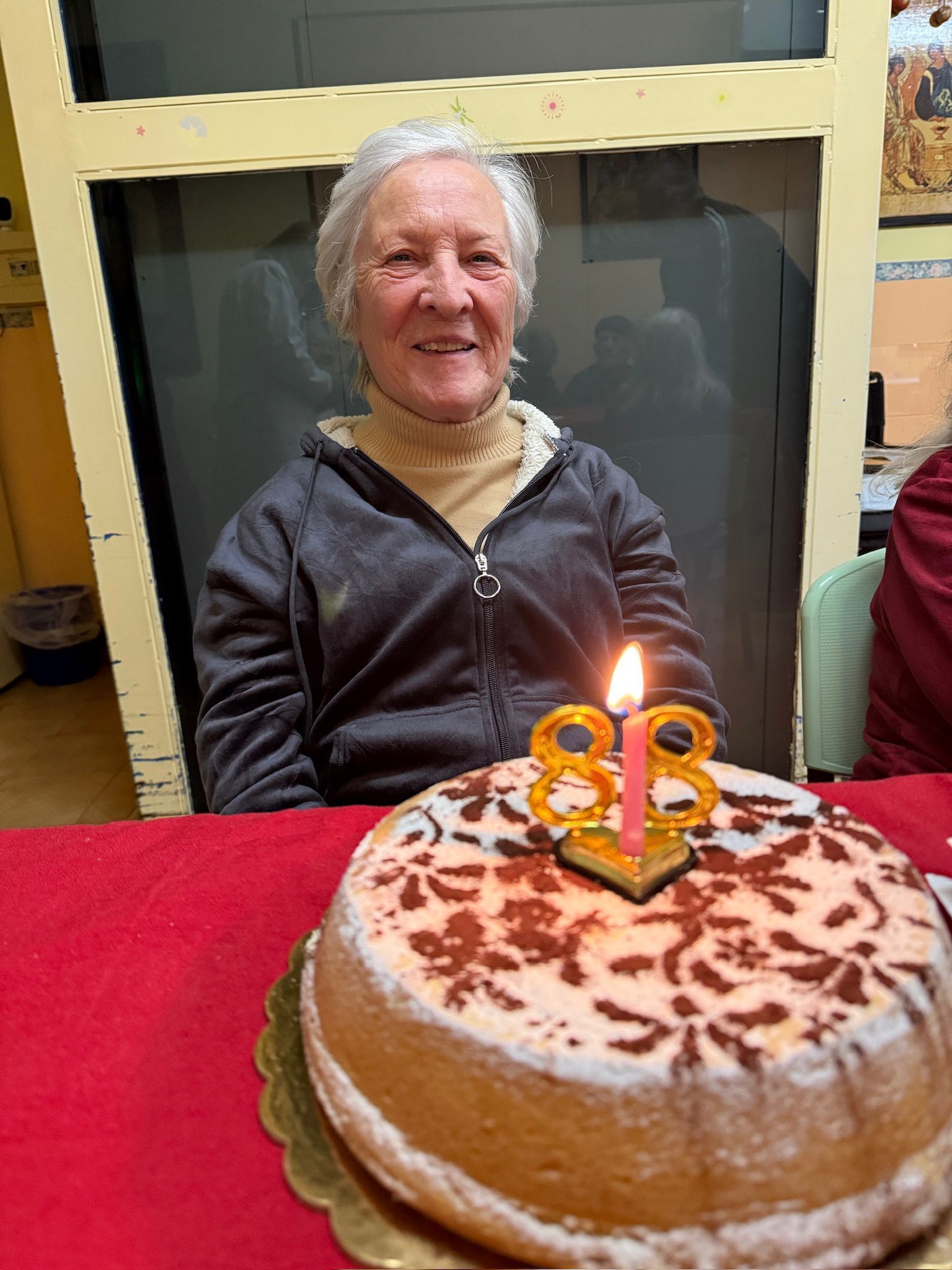 Donna seduta dietro una torta di compleanno con candeline accese su una tovaglia rossa