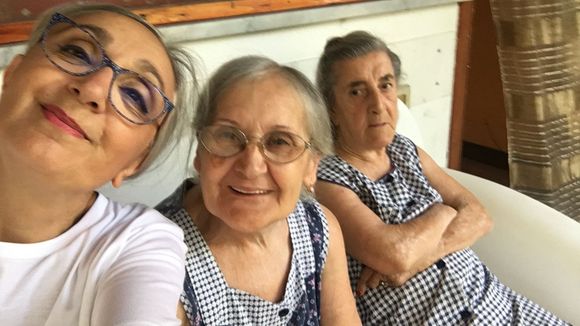 Due anziani sorridenti leggono un libro insieme su un divano luminoso.