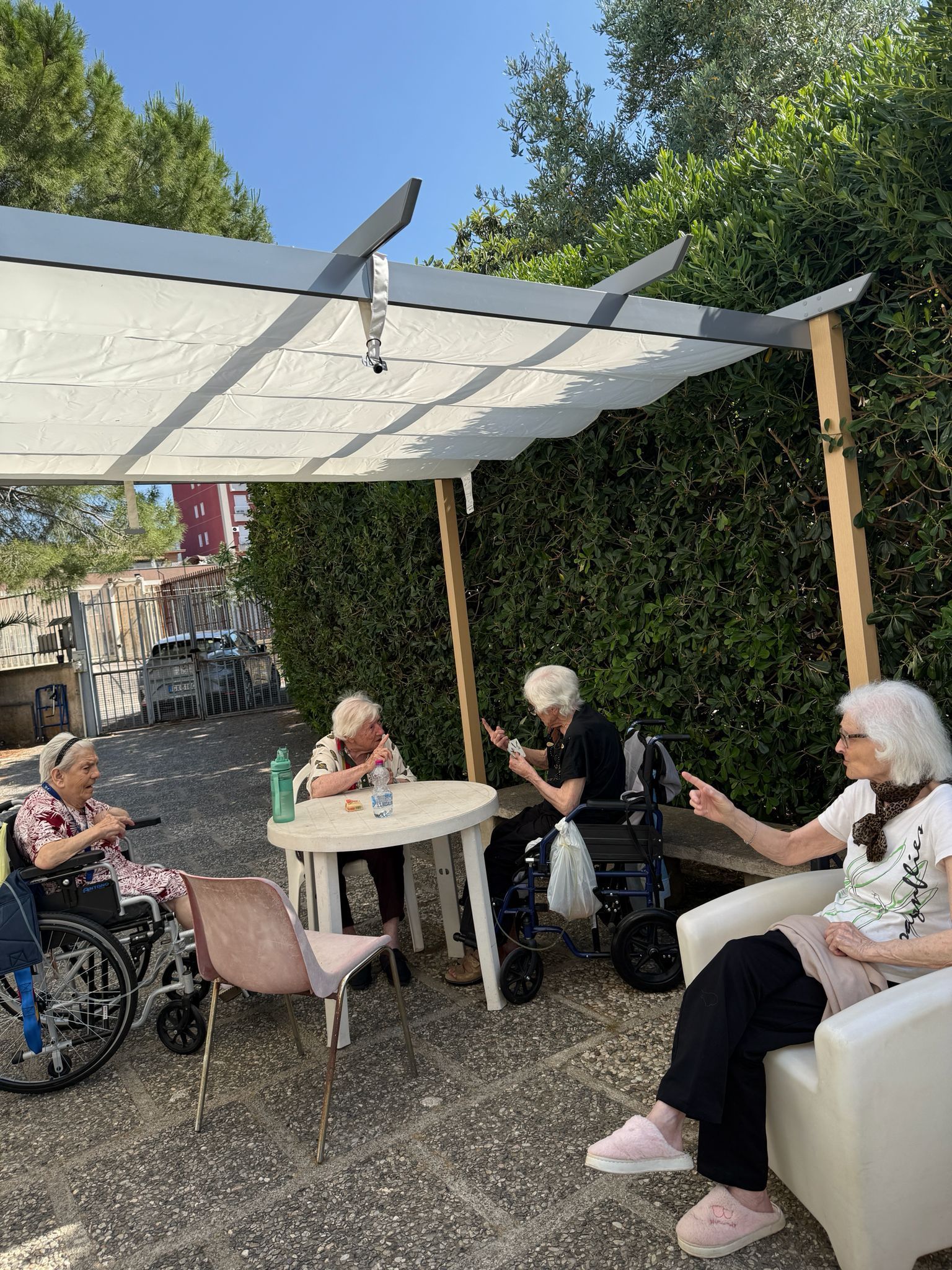 Persone sedute a chiacchierare sotto un baldacchino bianco in un soleggiato cortile del giardino.