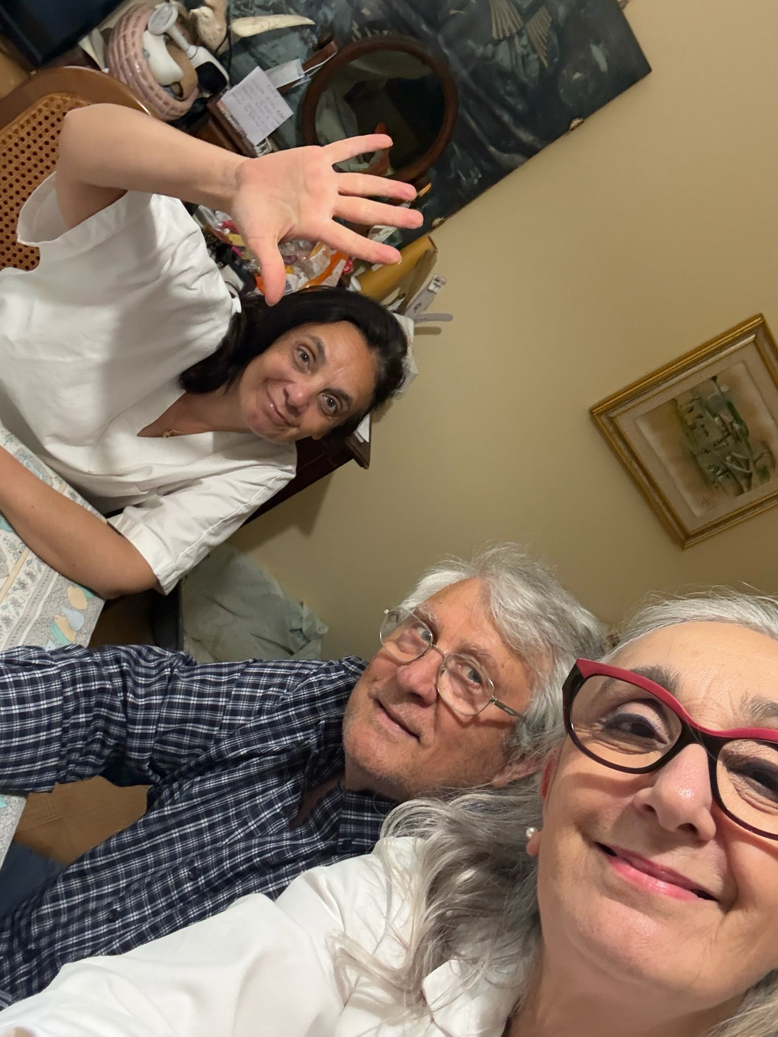 Tre persone sorridenti in un ambiente interno, una delle quali saluta con la mano la telecamera.