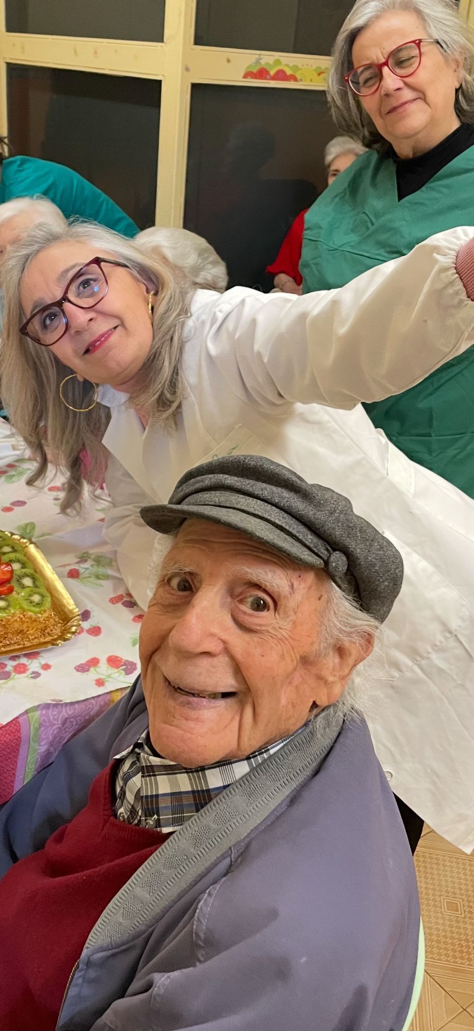 Tre persone sorridenti in posa durante una festa, una delle quali tiene in mano una torta in primo piano.