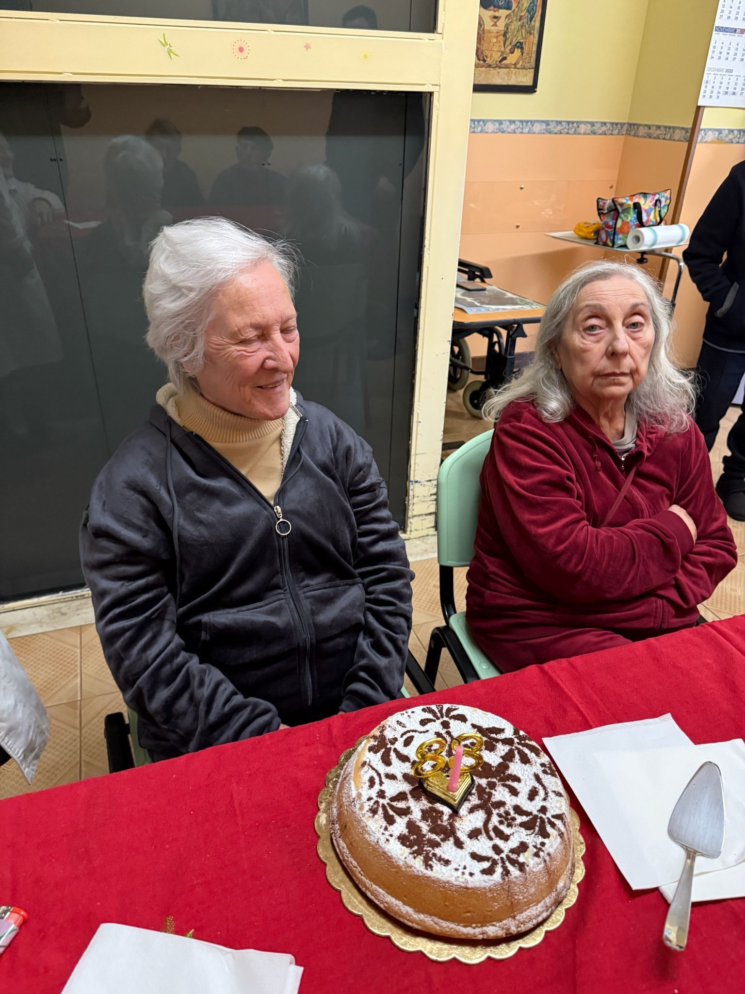 Due persone sedute a un tavolo con una torta decorata e una tovaglia rossa in una stanza