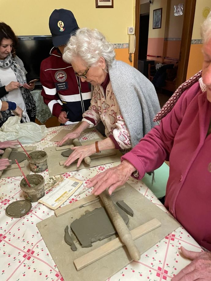 Persone che modellano l'argilla su un tavolo con strumenti e un modello, in un ambiente di laboratorio.