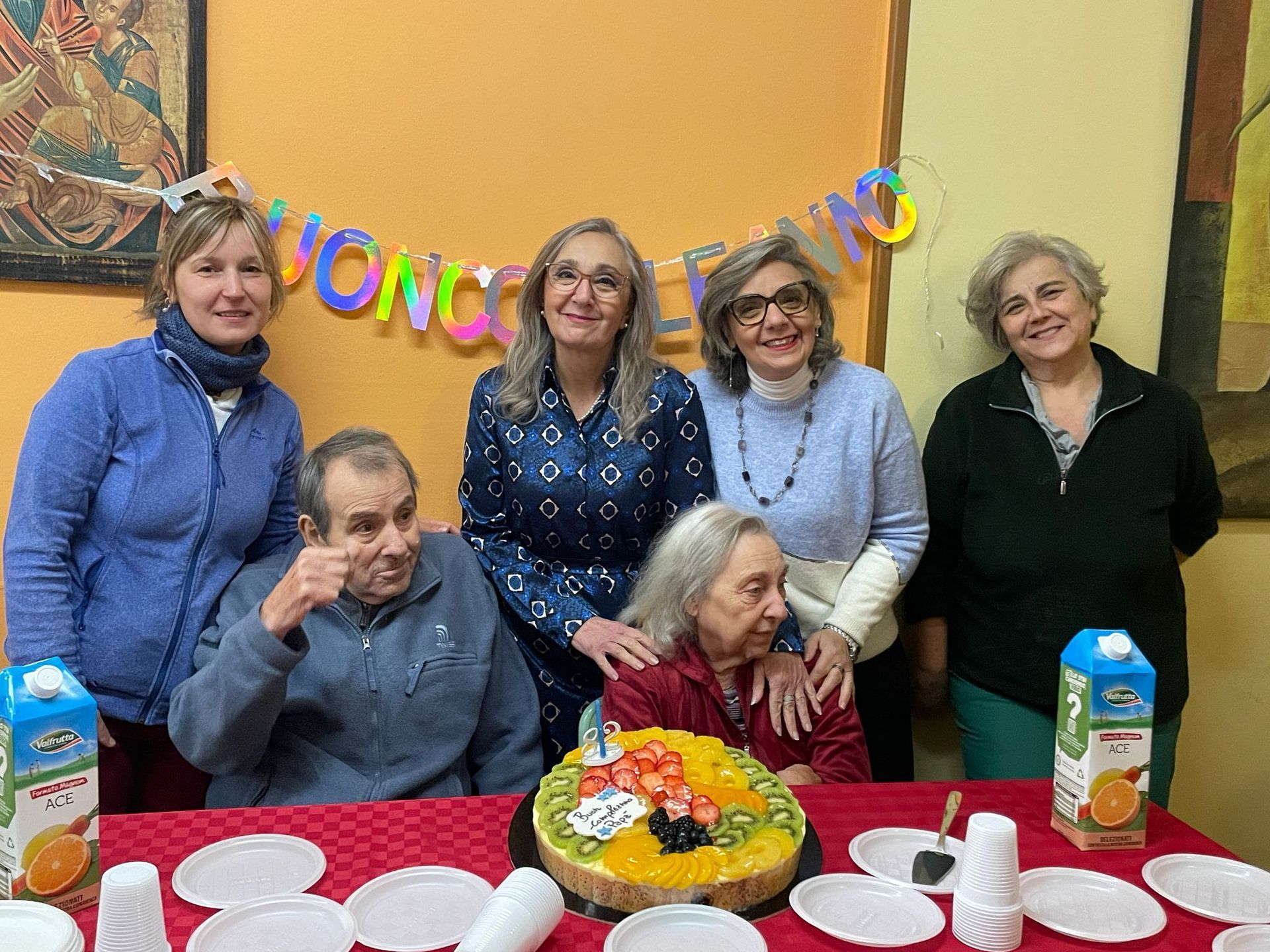 Il gruppo si è riunito attorno a un tavolo decorato con una torta di fiori, sorridendo durante una festa.