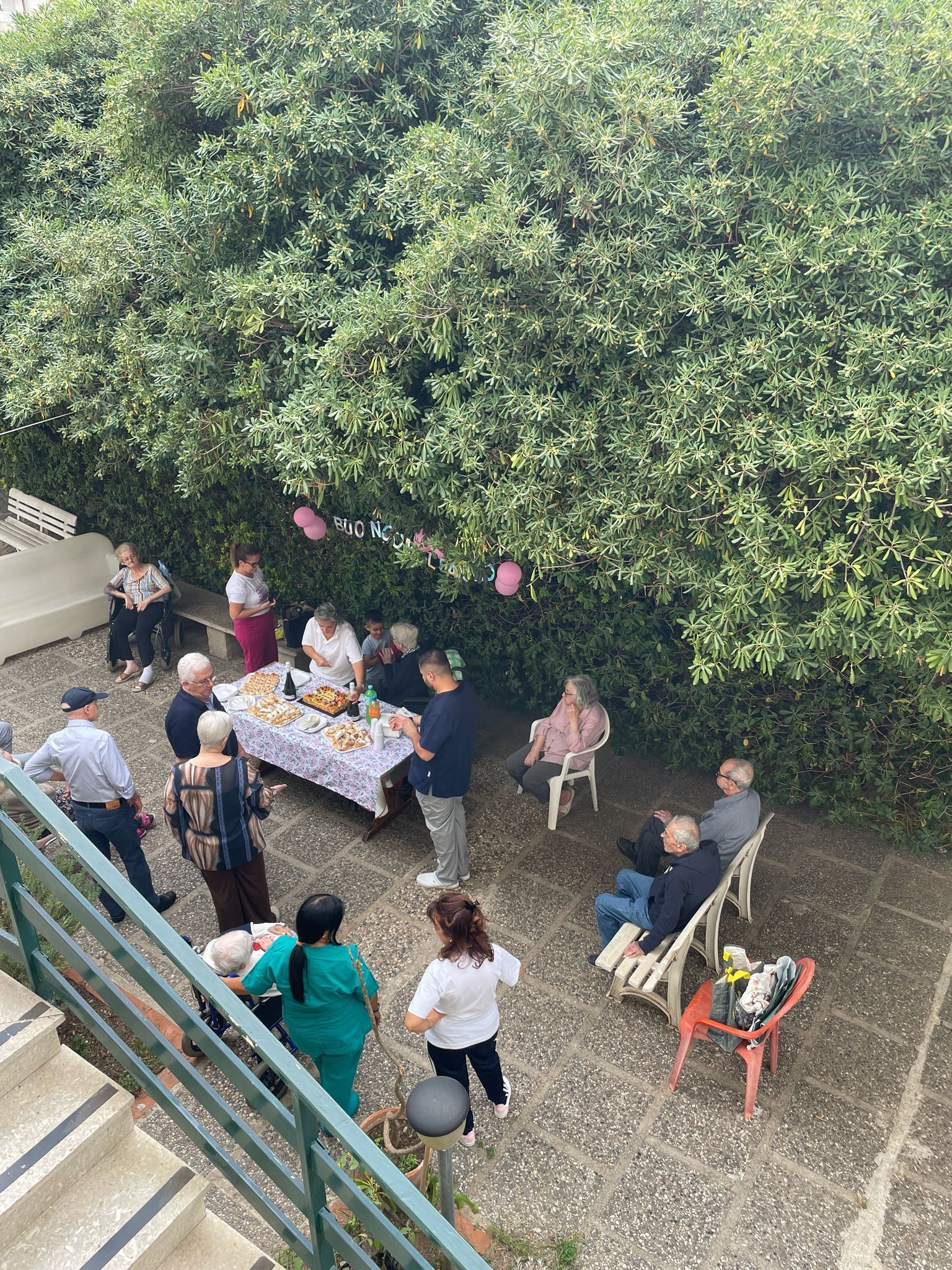 Le persone si sono riunite attorno a un tavolo all'aperto, sotto un grande albero, in un cortile.