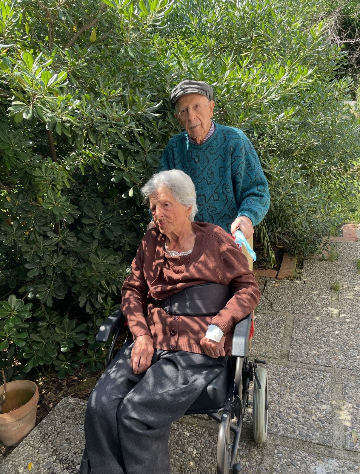 Due persone all'aperto, una seduta su una sedia a rotelle e l'altra in piedi dietro di lei su un sentiero del giardino.
