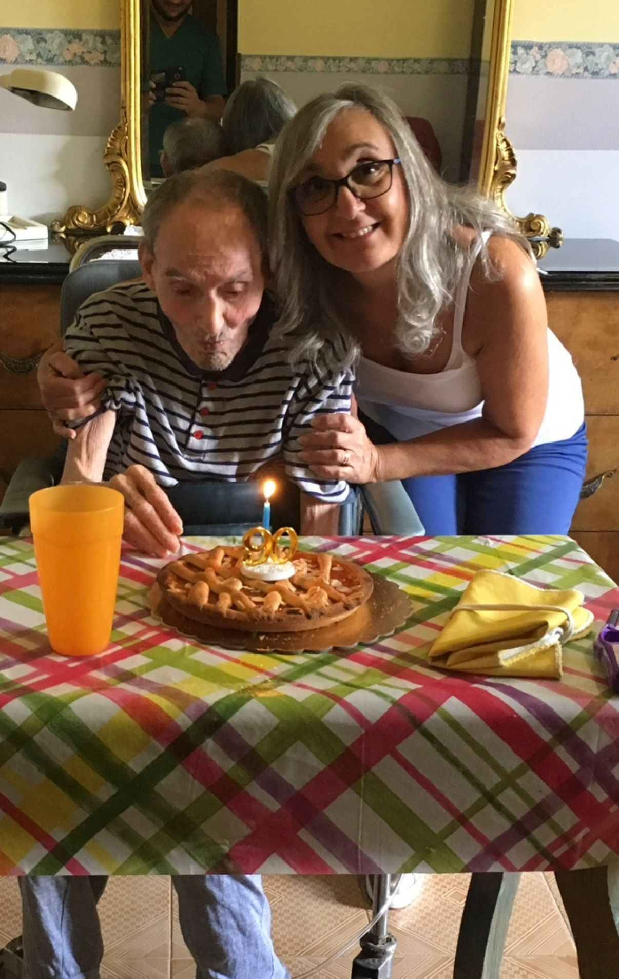 Due persone sedute a un tavolo, che condividono una torta di compleanno con le candeline accese nella sala da pranzo di casa.