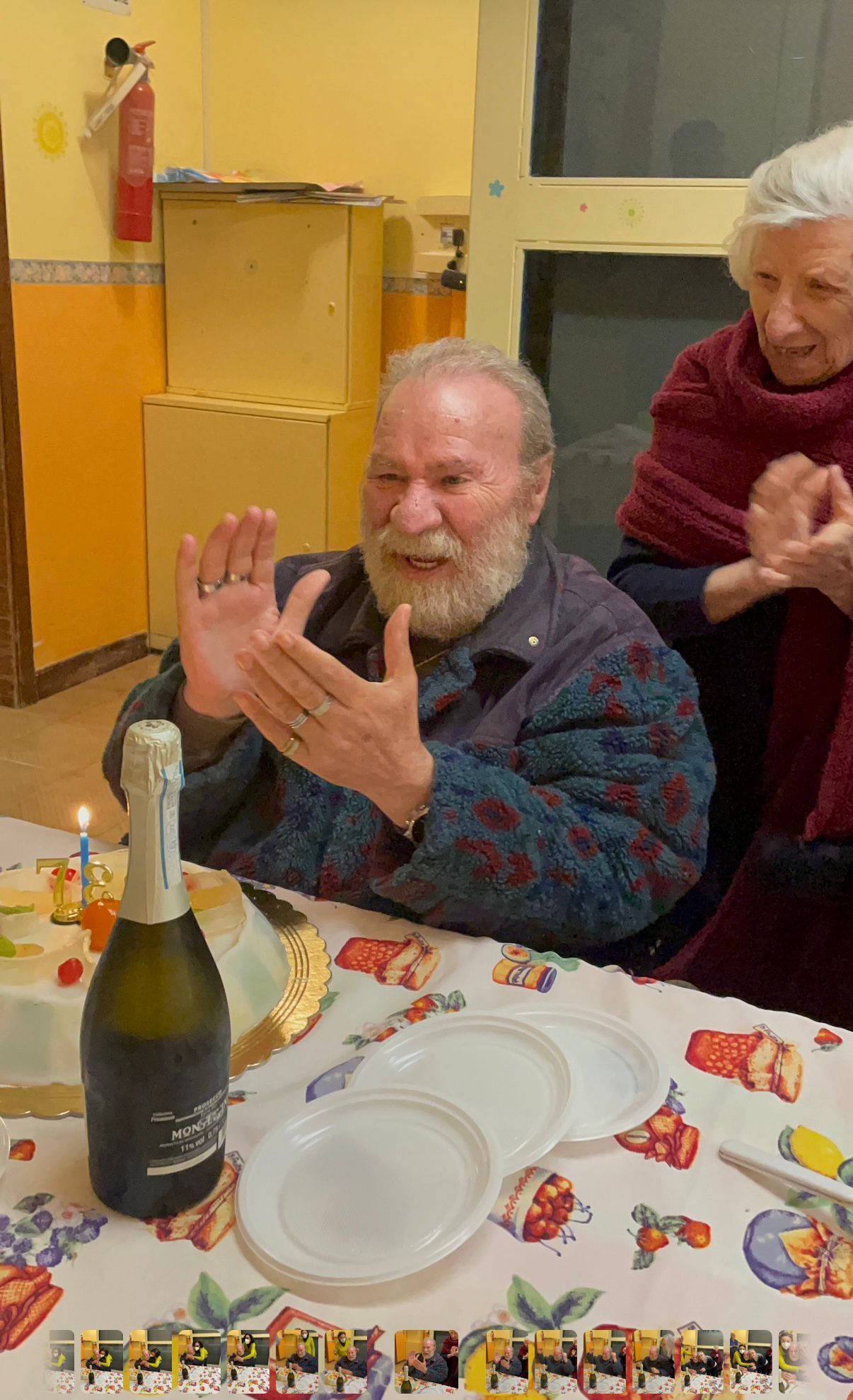 Due persone applaudono a un tavolo con una bottiglia di champagne e dei piatti, in una stanza decorata.