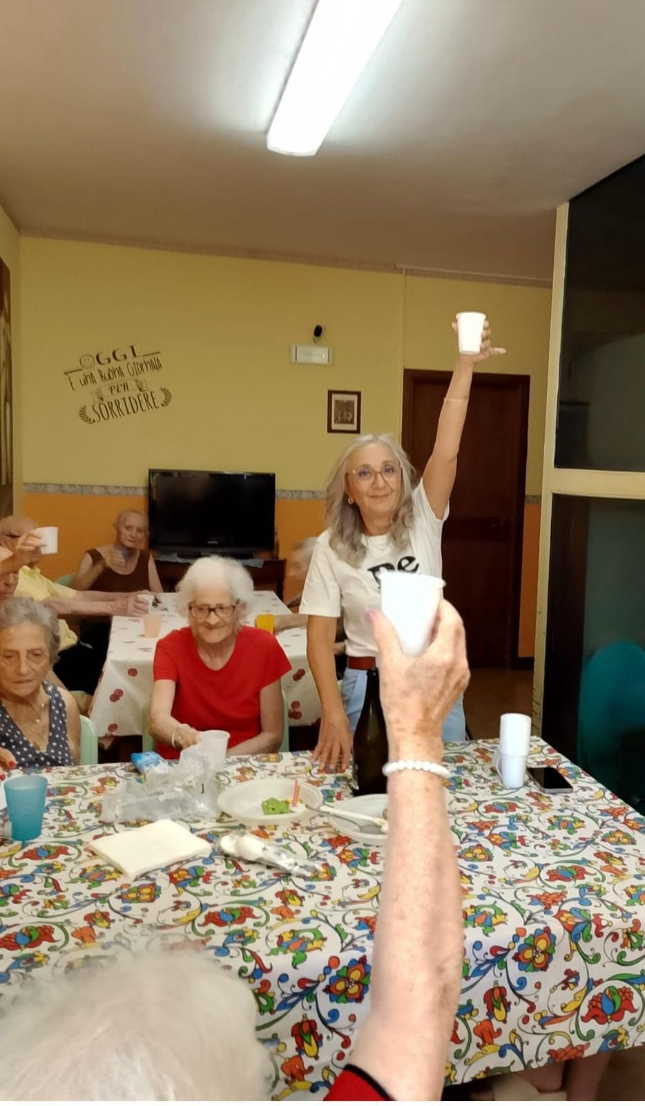 Persone sedute attorno a un tavolo in una stanza, con una persona in primo piano che tiene un braccio alzato.