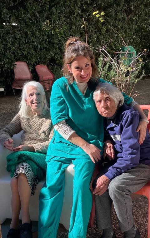 Due anziani sorridono e chiacchierano seduti in poltrona, uno dei due con un libro in mano, in un luminoso soggiorno.