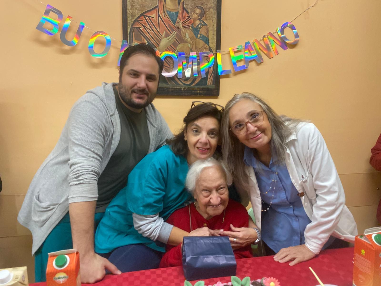 Quattro persone posano attorno a un tavolo di compleanno con uno striscione 