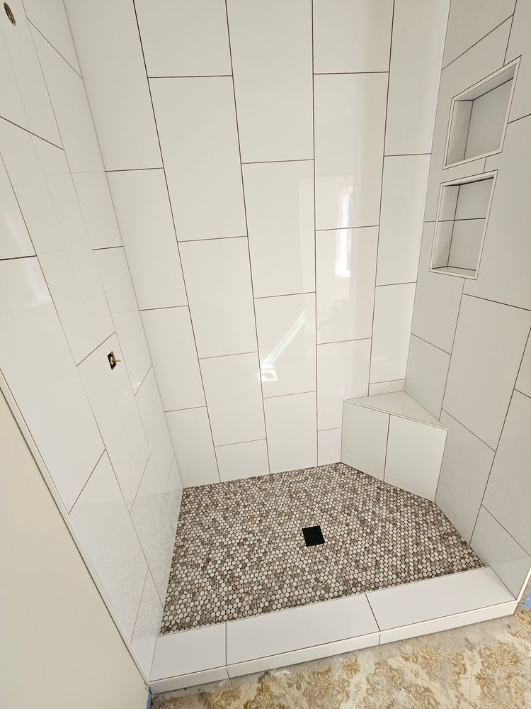 Shower with white tiled walls, mosaic tile floor, and corner seat.