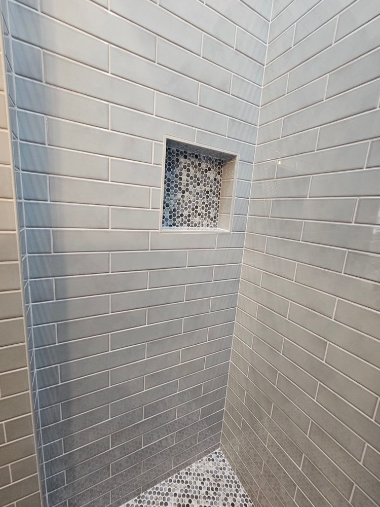 Gray tiled shower with a mosaic tiled alcove.